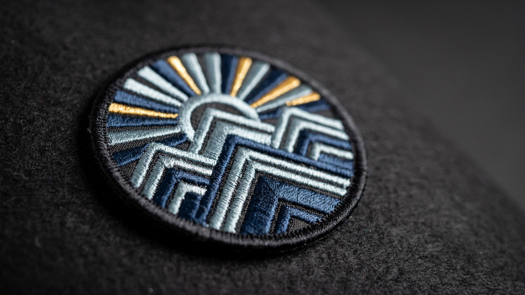 A round embroidered shader patch featuring blue, silver, and gold stitching to show light